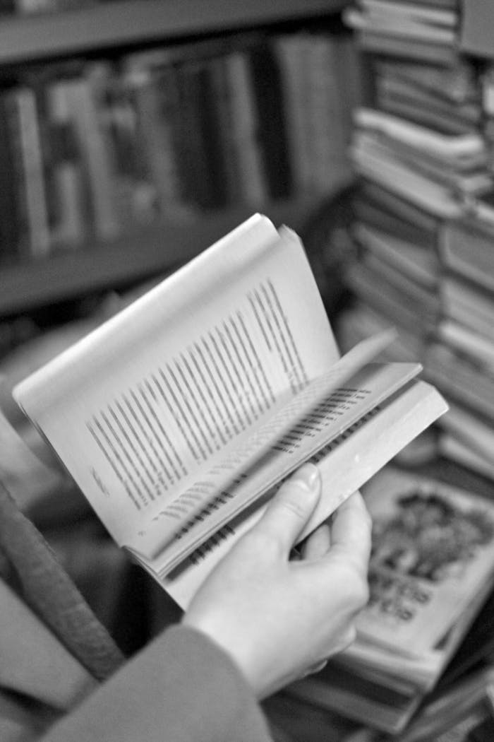 A detailed close-up of hands flipping through the pages of an open book in a monochrome setting.